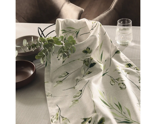 Runner de masă decorativ cu model floral pe o masă cu veselă și un pahar cu apă