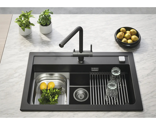 Chiuvetă de bucătărie neagră cu robinet, picurător și accesorii pe un blat de bucătărie.