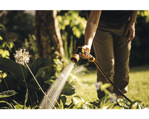 O persoană udă plantele din grădină cu un pulverizator de grădină.