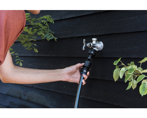 Persoană conectează un furtun de grădină la un robinet de apă exterior