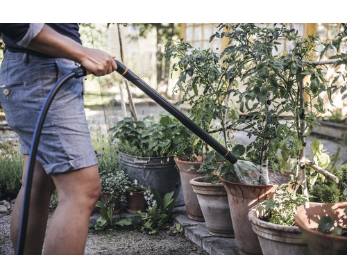 O persoană udă plantele în ghivece cu un pistol de pulverizare pentru grădină.