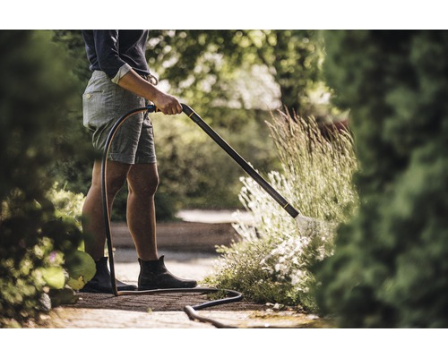 O persoană udă plante cu un aspersor de grădină în grădină.