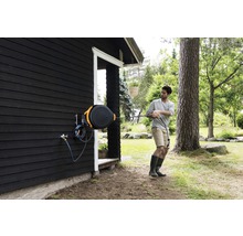 Persoană care trage un furtun de grădină dintr-o cutie de furtun de pe peretele unei case