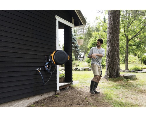 Persoană care trage un furtun de grădină dintr-o cutie de furtun de pe peretele unei case