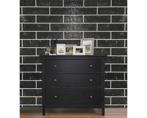 Comodă neagră cu trei sertare în fața unui perete cu modele de cărămidă neagră