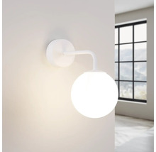 Lampa de perete albă cu glob de sticlă rotund în fața unei ferestre.