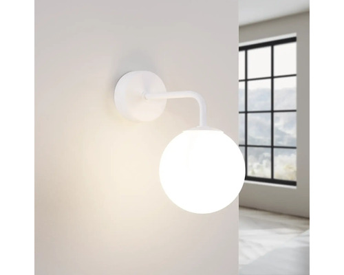 Lampa de perete albă cu glob de sticlă rotund în fața unei ferestre.