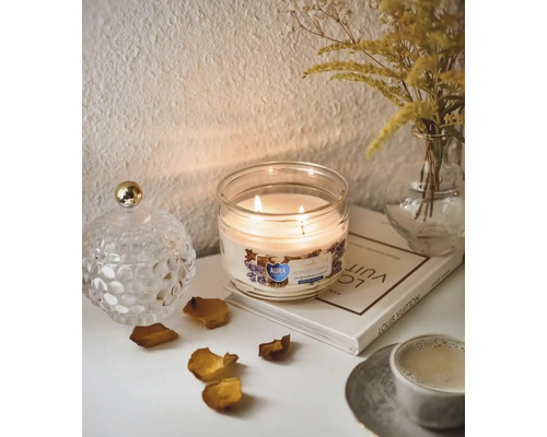 Scenă decorativă cu lumânare parfumată în pahar, vază cu flori și carte