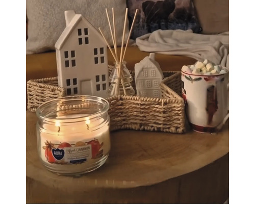 Aranjament decorativ cu lumânare, bețișoare parfumate, cană cu marshmallows și case pe o masă