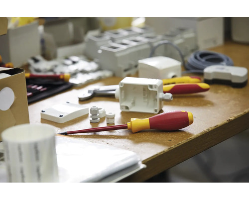 Fotografie cu scule și materiale pentru electricieni pe un banc de lucru, inclusiv șurubelnițe, carcase și prese de cablu