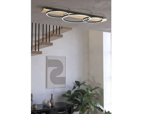 Interior modern cu o plafonieră LED cu trei inele, o scară și obiecte decorative.