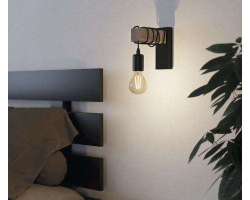 Lampa de perete cu elemente din lemn și metal lângă un pat