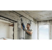Un bărbat taie o țeavă metalică cu un ferăstrău sabie într-o clădire în construcție.