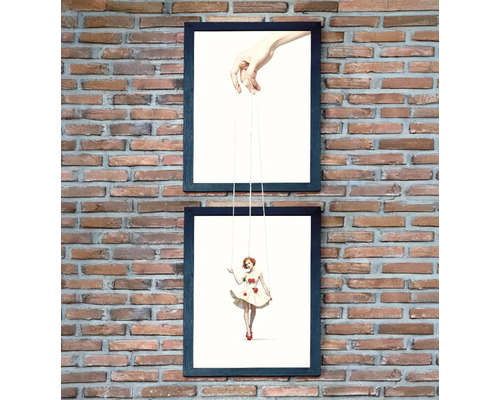 Două printuri artistice înrămate cu mâini și o figurină marionetă pe un perete de cărămidă