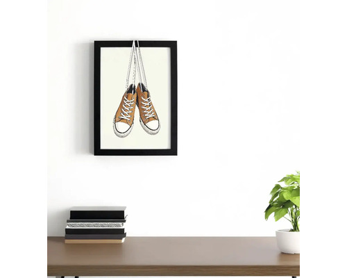 Imagine înrămată cu o pereche de adidași pe un perete deasupra unui birou cu cărți și o plantă.