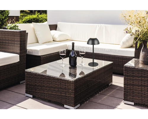 Scenă de exterior cu mobilier de ședere din ratan, măsuță de cafea cu blat de sticlă, sticlă de vin, pahare de vin și lampă de masă.