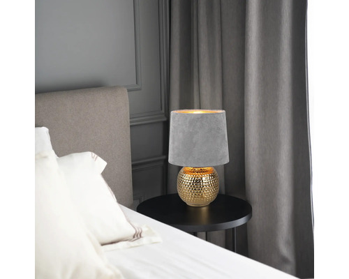 Lampă de noptieră cu abajur gri și bază aurie pe o masă