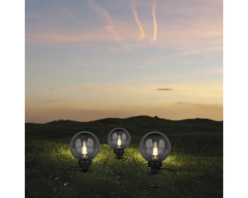 Trei lumini de grădină sferice cu cabluri de alimentare în iarbă la amurg