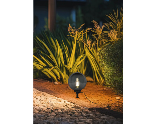 Scenă de grădină cu o lampă rotundă de exterior între plante și pietre.