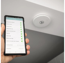 Un detector de fum este montat pe tavan în timp ce un smartphone cu un afișaj de setări este ținut în mână