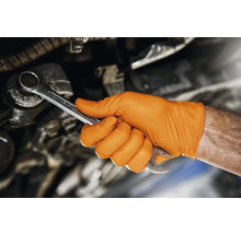 O mână cu o mănușă portocalie ține o cheie fixă.