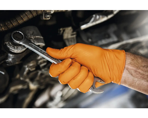 O mână cu o mănușă portocalie ține o cheie fixă.