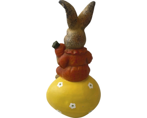 Iepure decorativ pe un ou de Paște cu un morcov în mână ca decorație de grădină