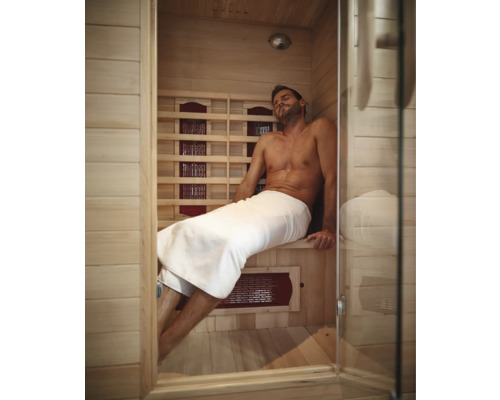 Bărbat relaxându-se într-o saună cu infraroșu cu pereți din lemn și ușă din sticlă