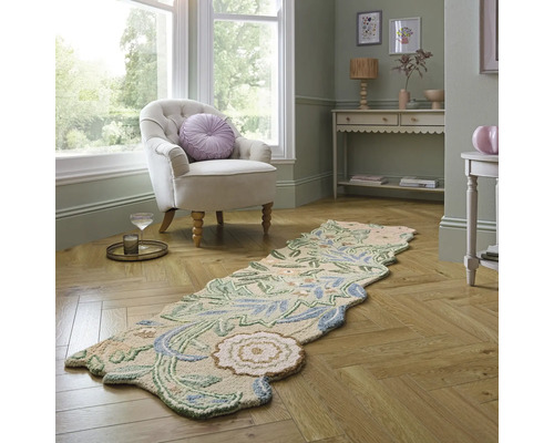 Cameră de zi decorativă cu un fotoliu bej, o masă decorativă și un covor cu model floral pe o podea de lemn.