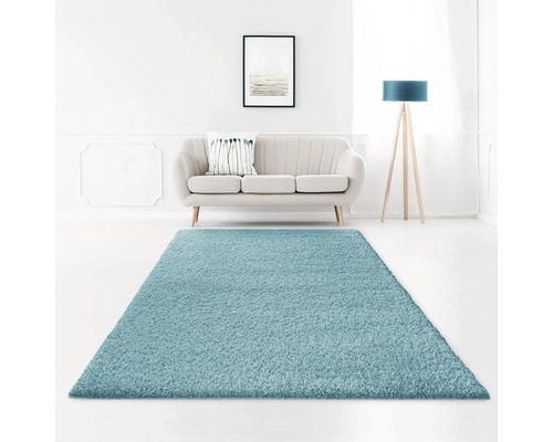 Covor pufos Shaggy Viva turcoaz 60x90 cm Un living cu o canapea, o lampă de podea și un covor cu fibre lungi