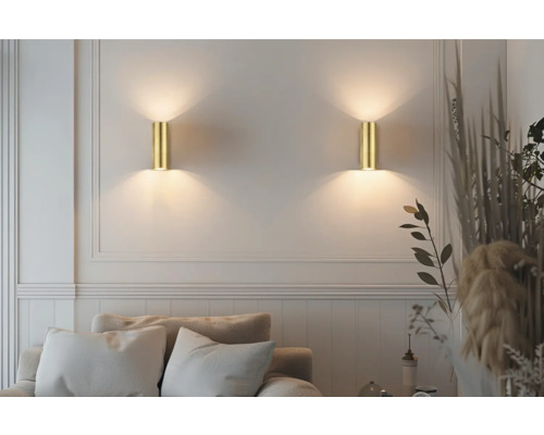 Două lămpi de perete aurii iluminează o zonă de living cu canapea și decorațiuni.