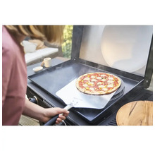 O persoană introduce o pizza pe un grătar cu ajutorul unei palete de pizza