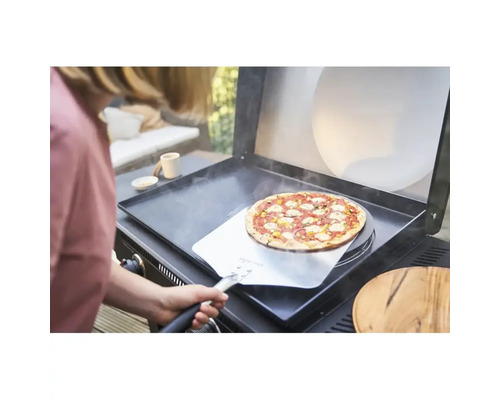 O persoană introduce o pizza pe un grătar cu ajutorul unei palete de pizza