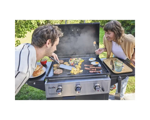 Două persoane pregătesc mâncare pe o plită Char-Broil, inclusiv legume, burgeri, ouă și bacon.