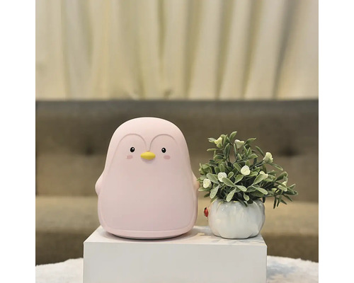 Lampă decorativă pinguin lângă o plantă în ghiveci