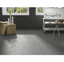 Baie cu gresie gri pe perete și podea, scaun de lemn deschis la culoare, masă și fereastră