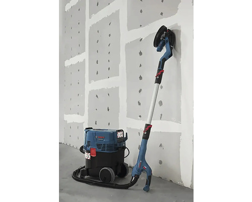 Șlefuitor de perete cu aspirator în fața unui perete