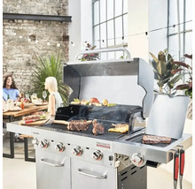 Grătar pe gaz cu alimente la grătar într-un mediu luminos, cu un perete de cărămidă și persoane așezate