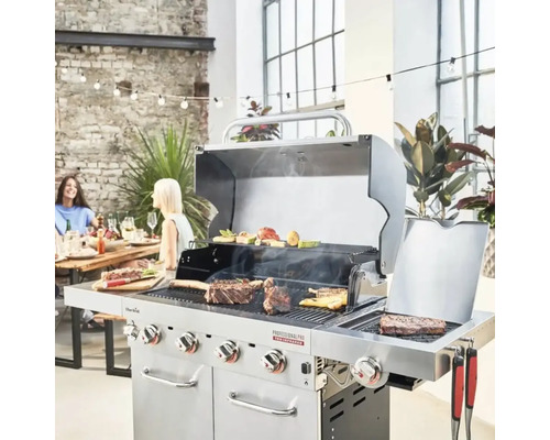 Grătar pe gaz cu alimente la grătar într-un mediu luminos, cu un perete de cărămidă și persoane așezate