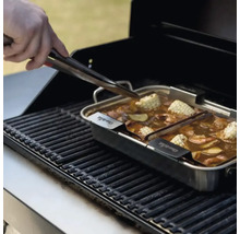 Grătar cu creveți, porumb și legume într-o tigaie din oțel inoxidabil, o mână folosește un clește.