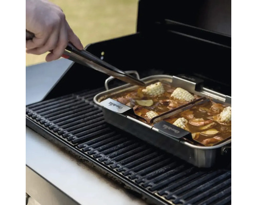 Grătar cu creveți, porumb și legume într-o tigaie din oțel inoxidabil, o mână folosește un clește.