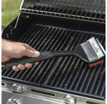 O mână folosește o perie de grătar pentru a curăța un grătar.