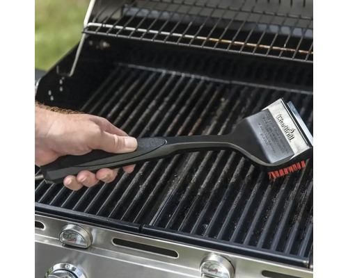 O mână folosește o perie de grătar pentru a curăța un grătar.