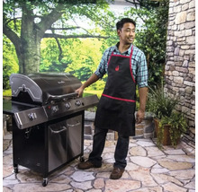 Bărbat cu șorț de grătar stând lângă un grătar pe gaz în grădină.