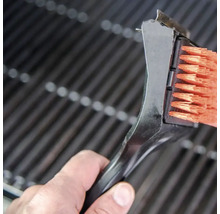 O perie de grătar cu racletă curăță un grătar.