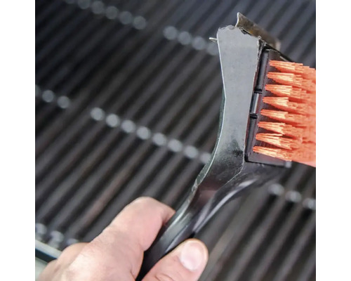 O perie de grătar cu racletă curăță un grătar.