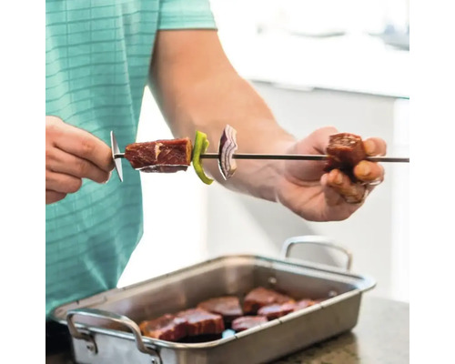 O persoană pune carne, ardei și ceapă pe o frigăruie.