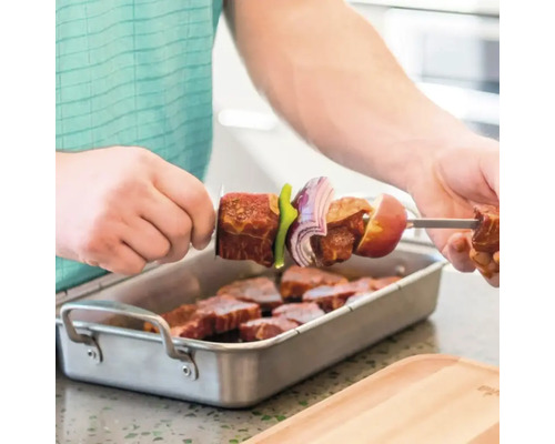 Bărbat înșirând carne și legume pe o frigăruie deasupra unui vas cu bucăți de carne