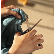 Persoană care taie material textil cu o foarfecă de modelare.