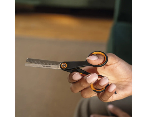 O mână ține o foarfecă de filat marca Fiskars.